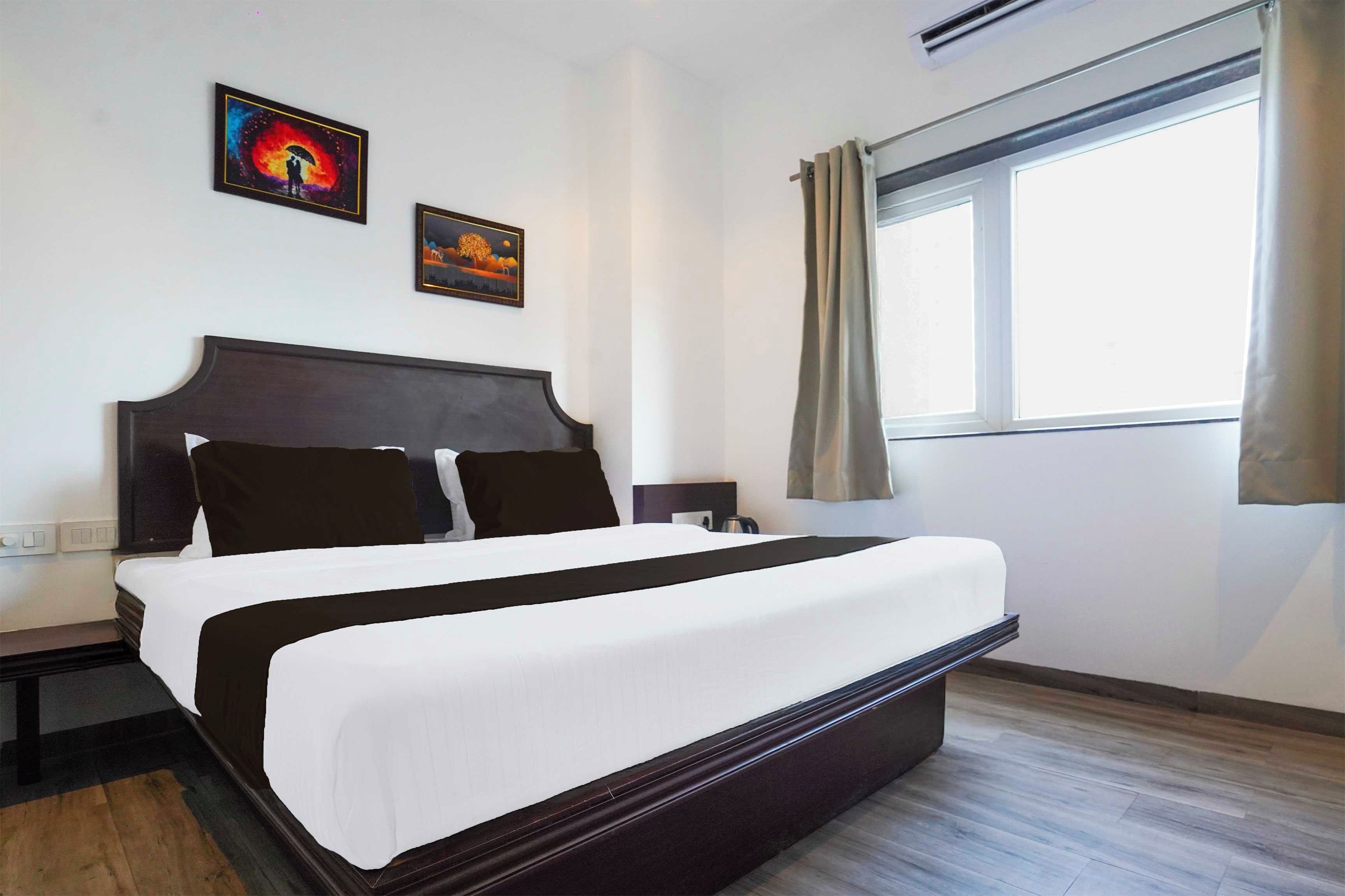 A hotel room with a large bed, two bedside tables, a window with curtains, and two wall-mounted artworks.