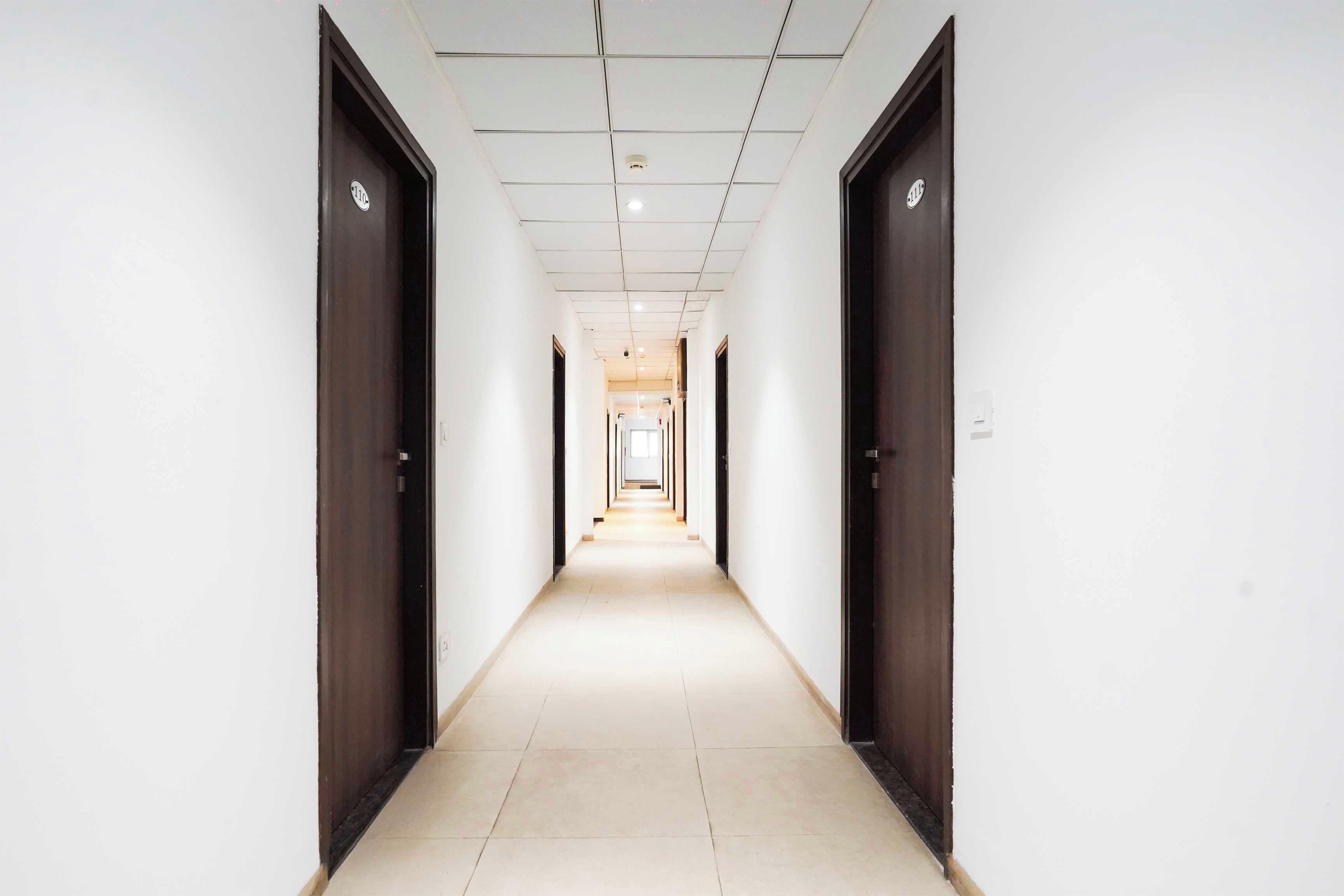 A long, narrow hallway with doors on both sides leading to rooms. The hallway has a tiled floor and a ceiling with recessed lighting.