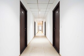 Un long couloir étroit, avec des portes des deux côtés menant à différentes pièces. Le couloir est doté d’un sol carrelé et d’un plafond avec des spots encastrés.
