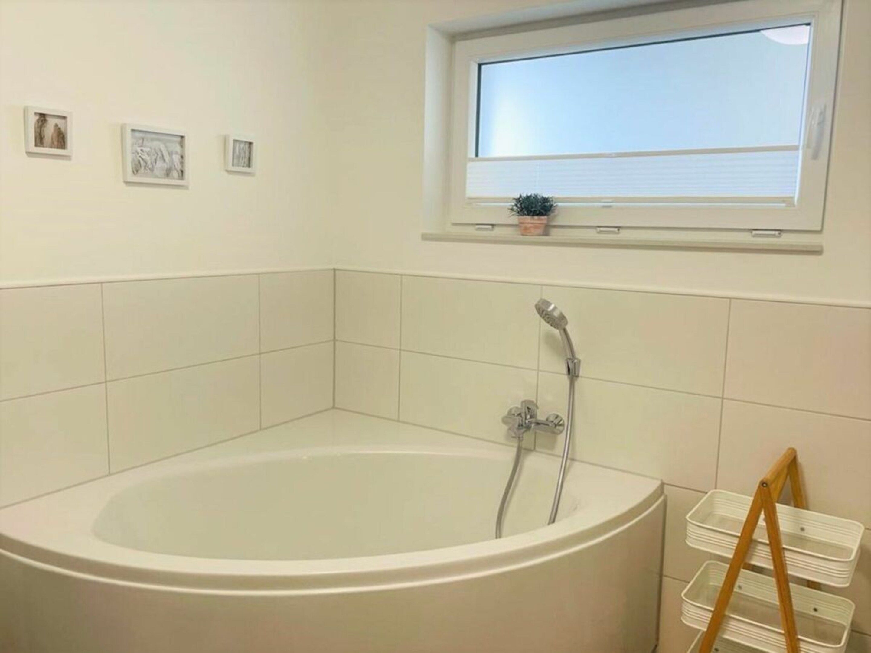 Un bany amb banyera autònoma, una finestra sobre el lavabo i una petita planta al davant de la finestra.