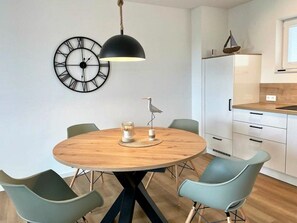 A modern kitchen with white cabinets, a wooden dining table, and a round clock on the wall. - 49.5m Anchorage (Wangerland)