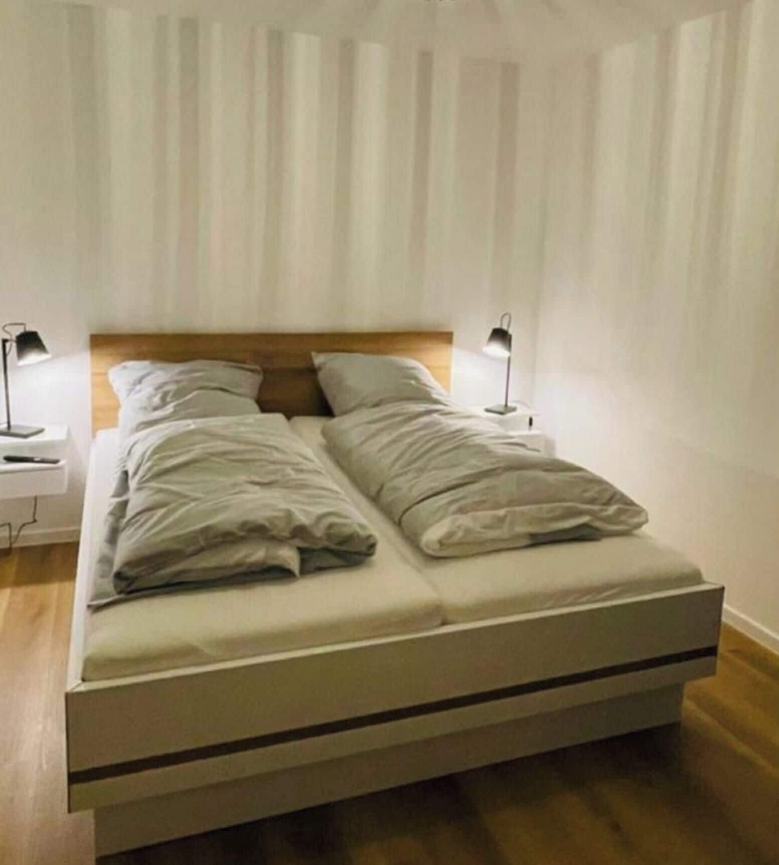 Un lit simple avec une tête de lit en bois, deux lampes de chevet et un matelas blanc.