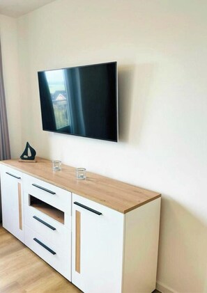 A modern living room with a flat-screen TV mounted on the wall, a wooden cabinet with drawers, and a glass on the cabinet's surface. - 49.5m Anchorage (Wangerland)