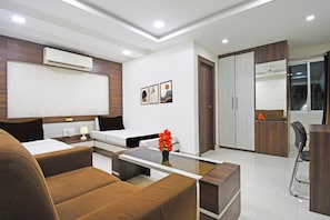 A modern hotel room with a bed, a desk, a chair, a sofa, and a bathroom with a mirror and wardrobe.