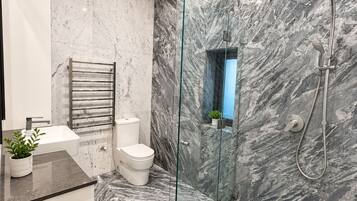 A modern bathroom with a glass-enclosed shower, a white toilet, and a marble-tiled floor.