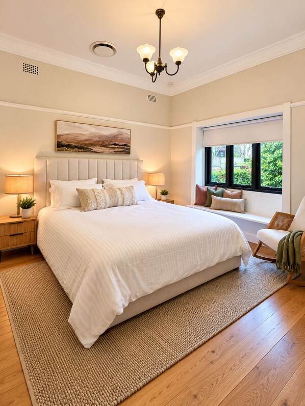 A bedroom with a large bed, a headboard, bedside lamps, a window with a view, and a hanging light fixture.