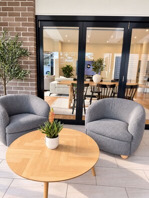 A modern interior with a round wooden table, two grey armchairs, and a potted plant.