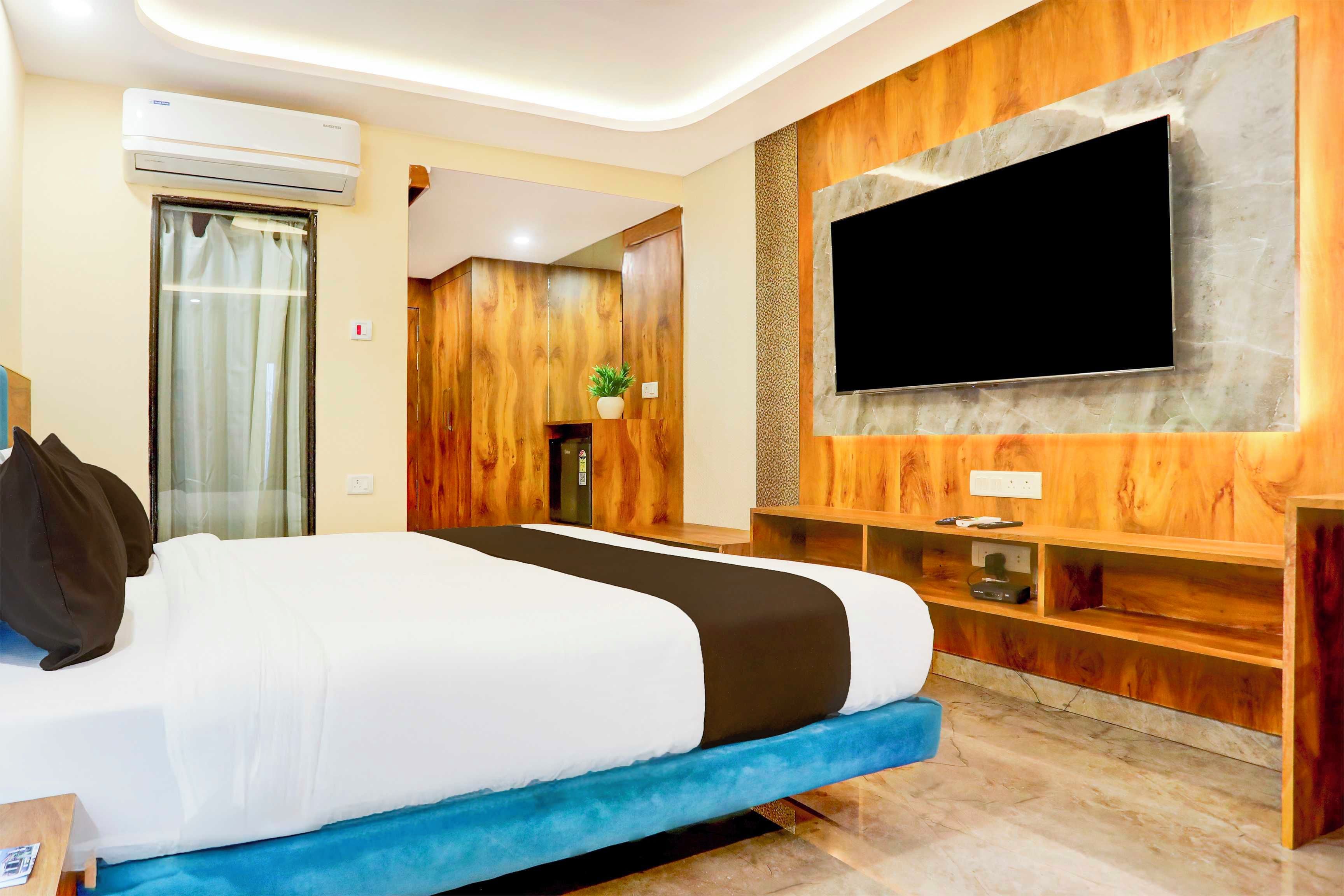 Habitación de hotel con cama, televisor de pantalla plana en la pared, diseño de paneles de madera, una planta pequeña y una ventana con cortinas.
