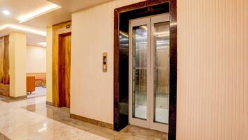 Un pasillo con una puerta de madera, un ascensor de vidrio y un cartel con un número encima de la puerta.