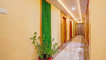 A hotel hallway with a green vertical garden, wooden doors, and a potted plant with pink flowers.