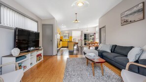 Ein modernes Wohnzimmer mit Flachbildfernseher, einer Couch und einer Essecke mit Tisch und Stühlen.