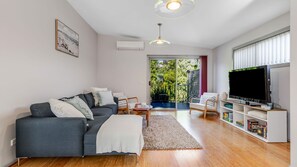 Ein modernes Wohnzimmer mit einem grauen Sofa, einem Fernseher und einem Bücherregal.