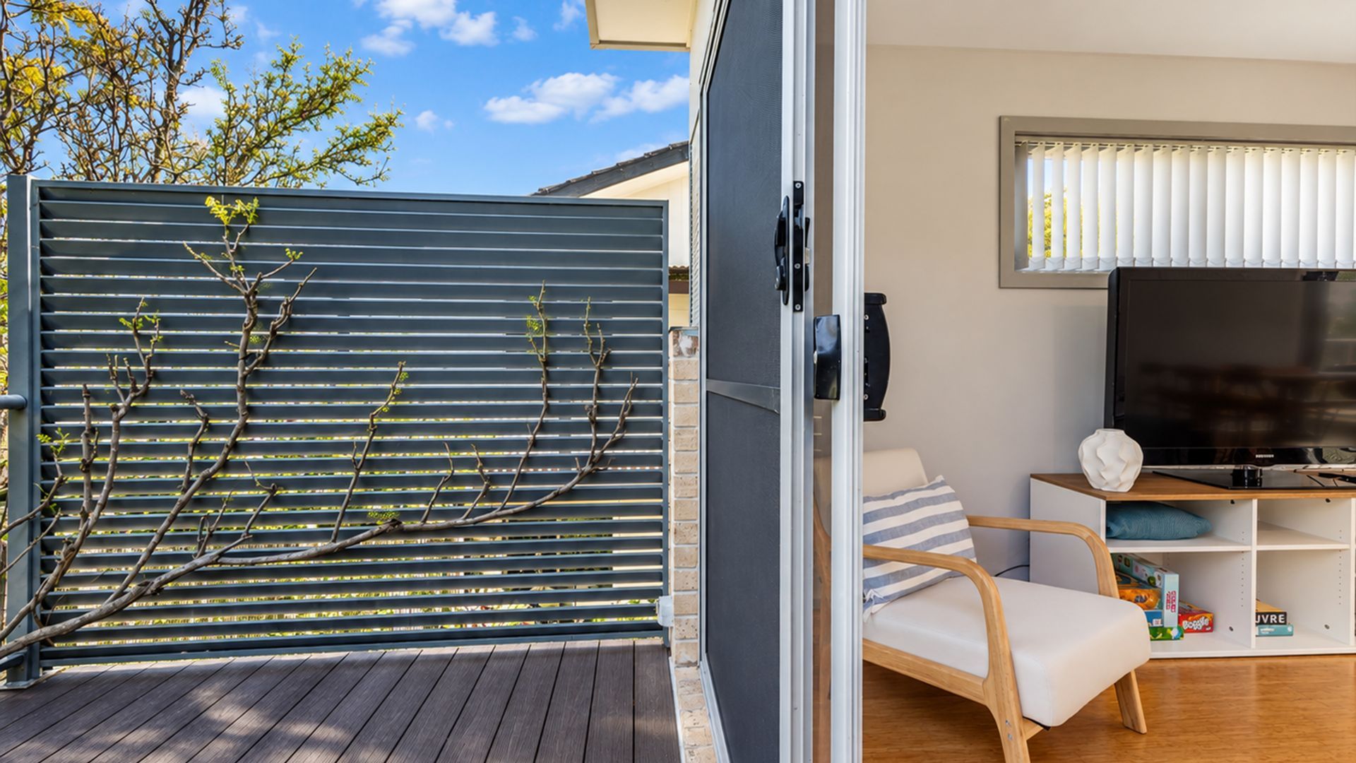 A modern outdoor seating area with a wooden deck, a grey metal fence, and a television set on a wooden stand.