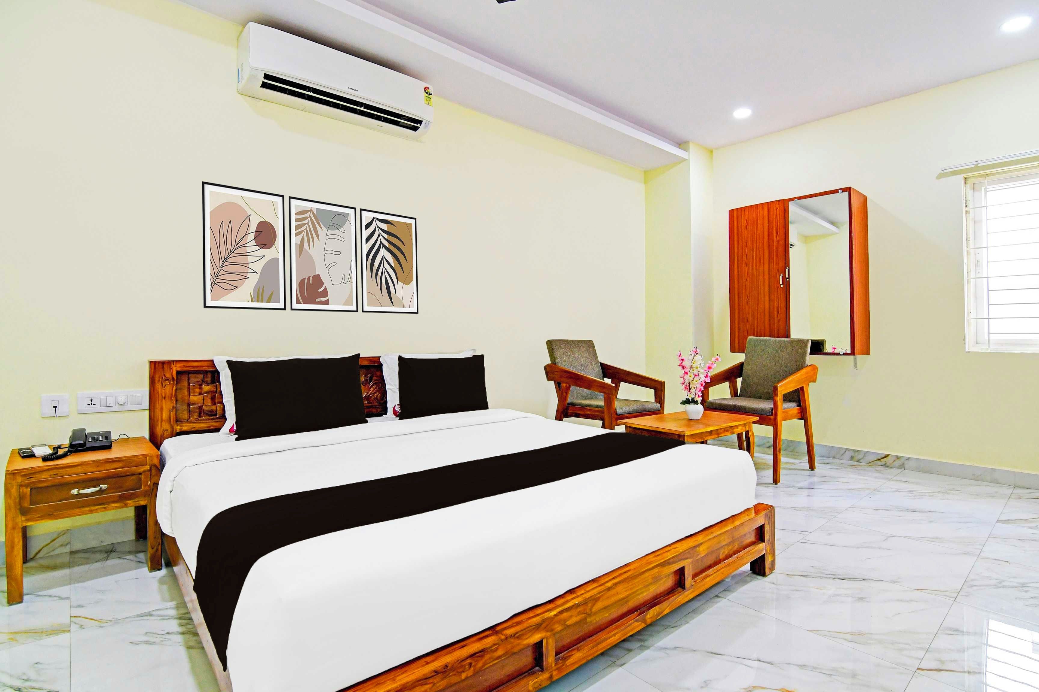 A hotel room with a bed, a desk with a phone, a chair, a mirror, and wall art.