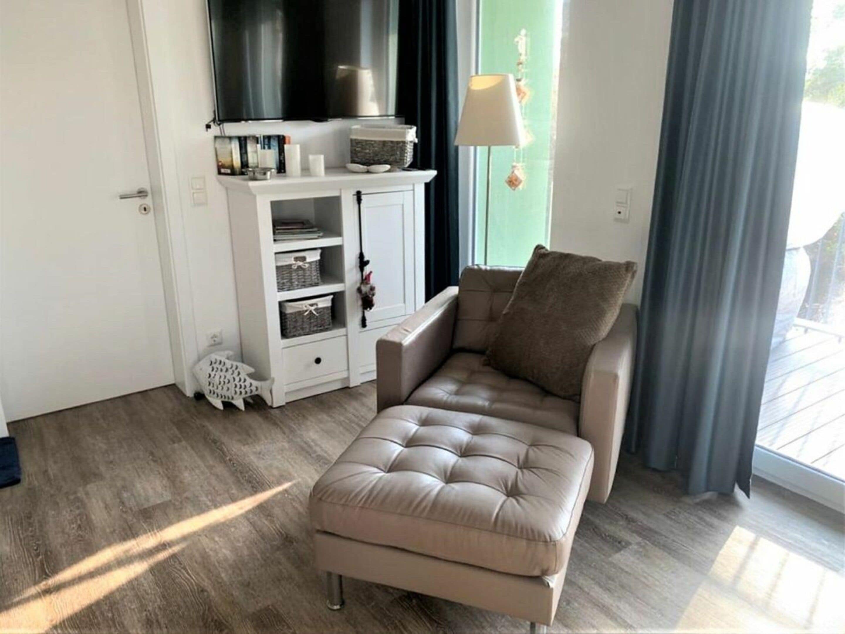 A modern living room with a beige sofa, a white cabinet with storage, and a large window with curtains.