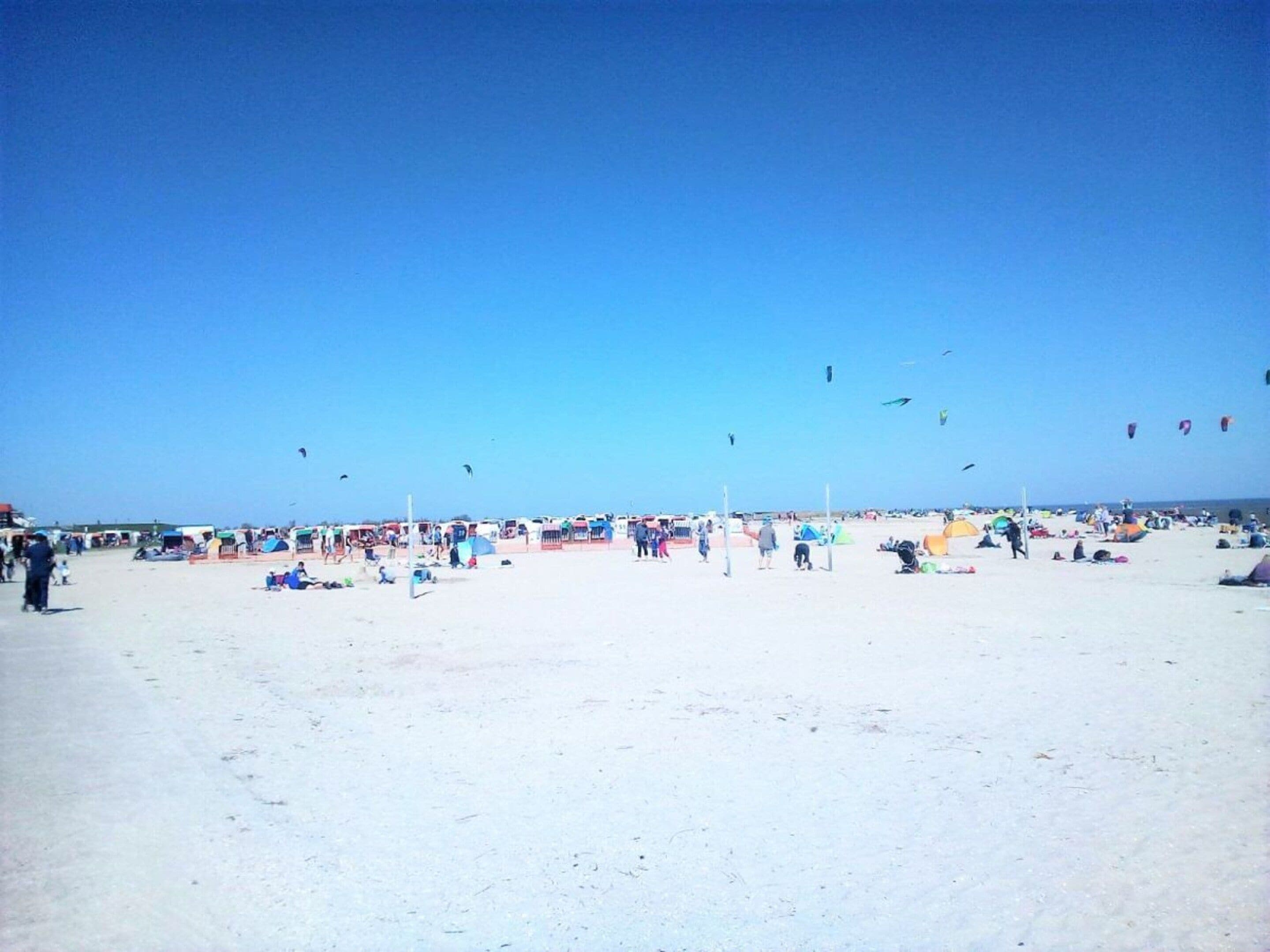 Platja amb tendes, gent, cel serena i quioscos volant.