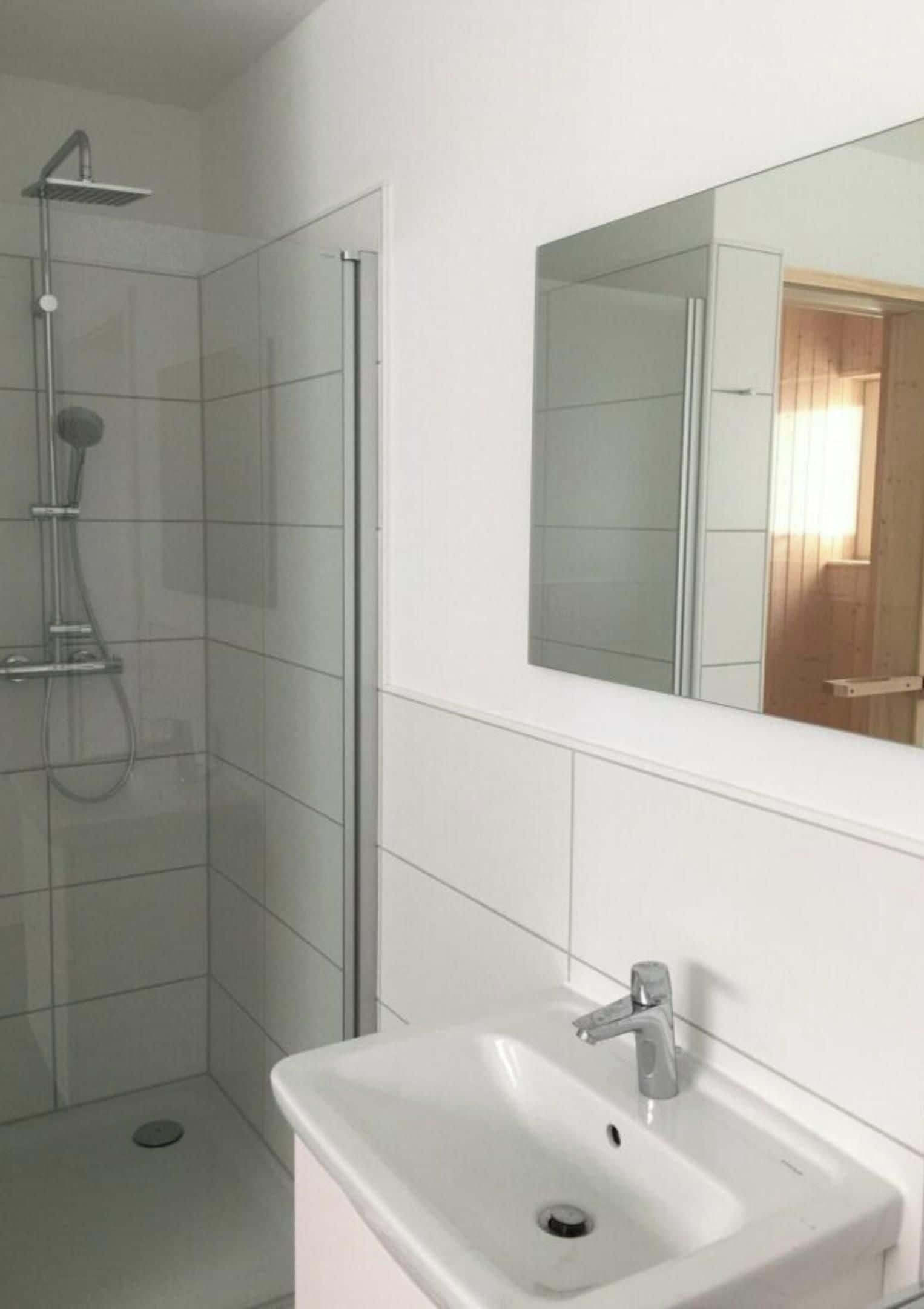Un baño con ducha, lavamanos y espejo.