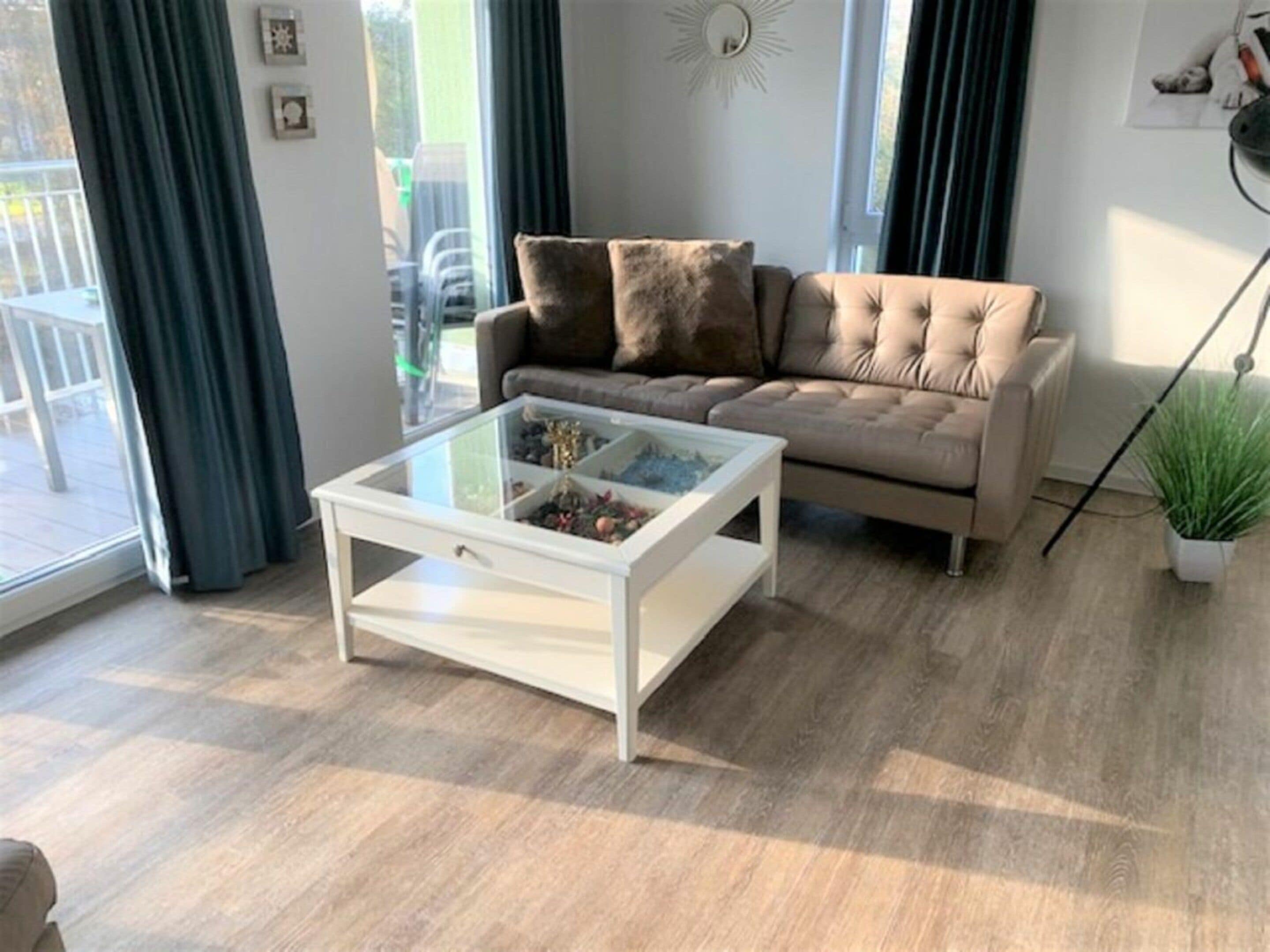 Ett vardagsrum med en beige soffa, ett soffbord i glas och en krukväxt.
