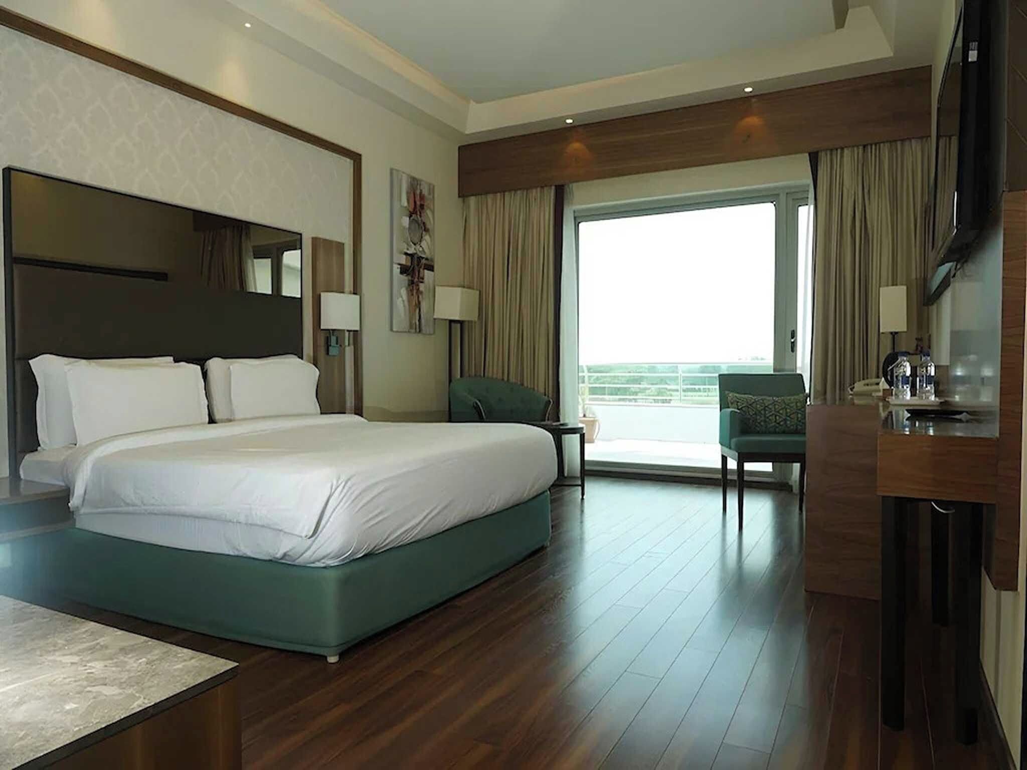 A hotel room with a large bed, a desk, a chair, and a balcony.