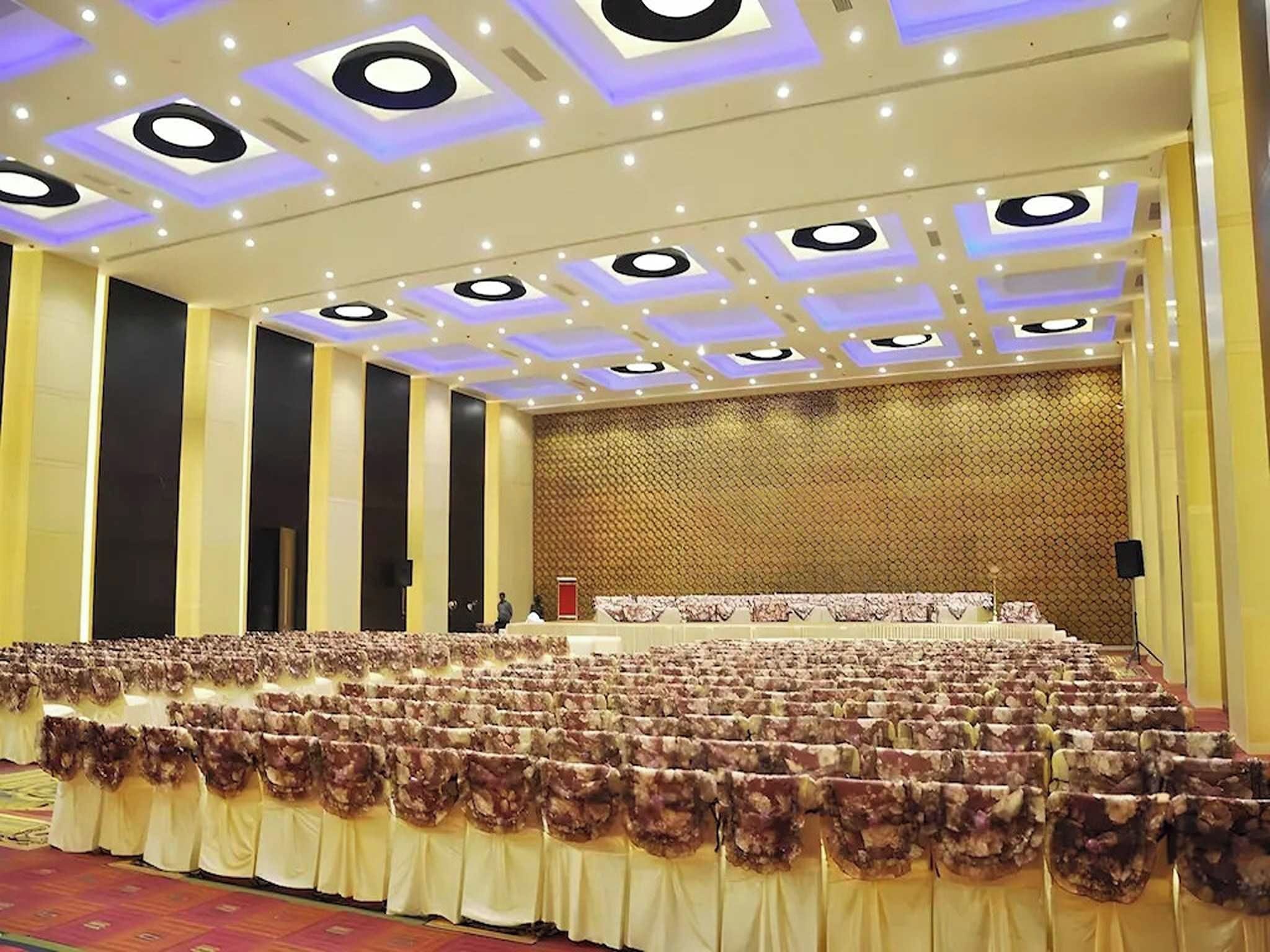 A large hall with tiered seating, a stage, and a patterned wall.