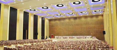 A large hall with tiered seating, a stage, and a patterned wall.