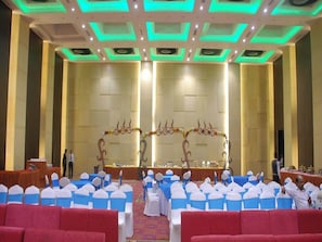 A conference room with rows of chairs, a stage with a floral arch, and a modern ceiling design.