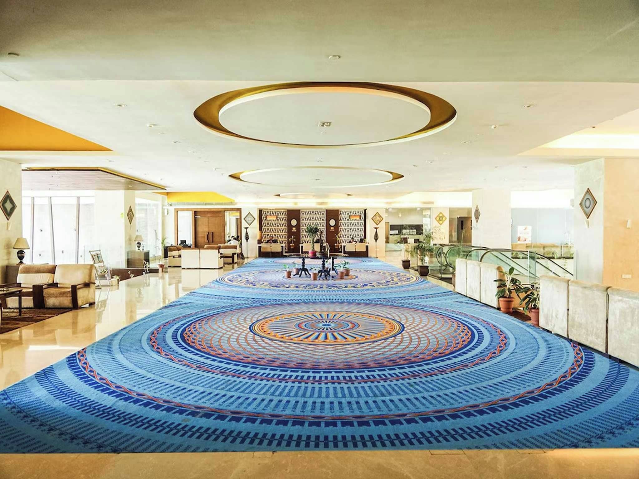 A spacious lobby with a patterned carpet, a reception desk, and a staircase.