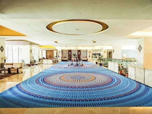A spacious lobby with a patterned carpet, a reception desk, and a staircase.