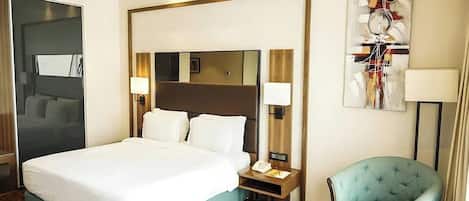 Une chambre d’hôtel avec un grand lit, des tables de chevet, une chaise, une petite table et un tableau au mur.