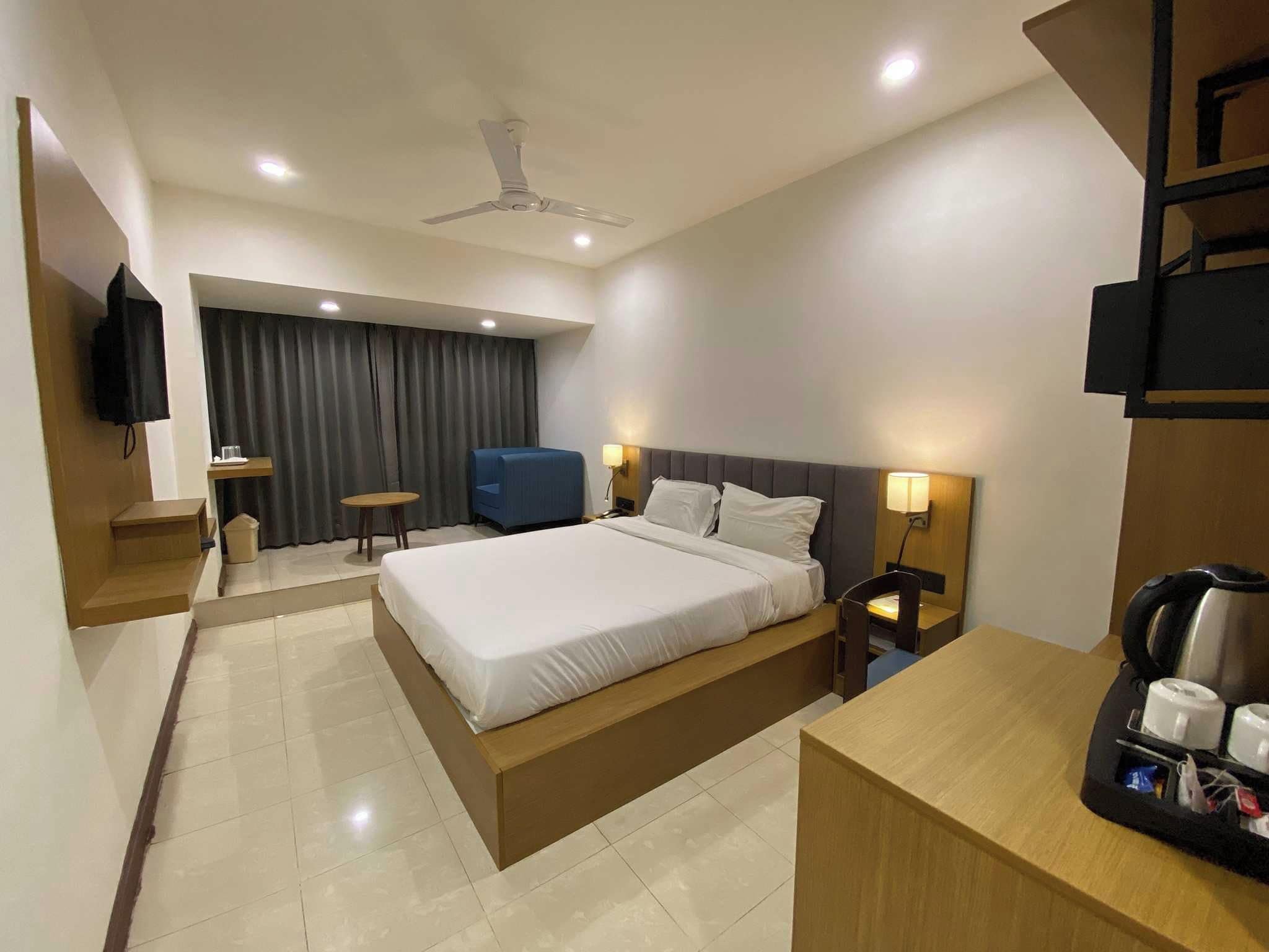 A hotel room with a bed, bedside tables, a desk, a chair, a television, and a ceiling fan.