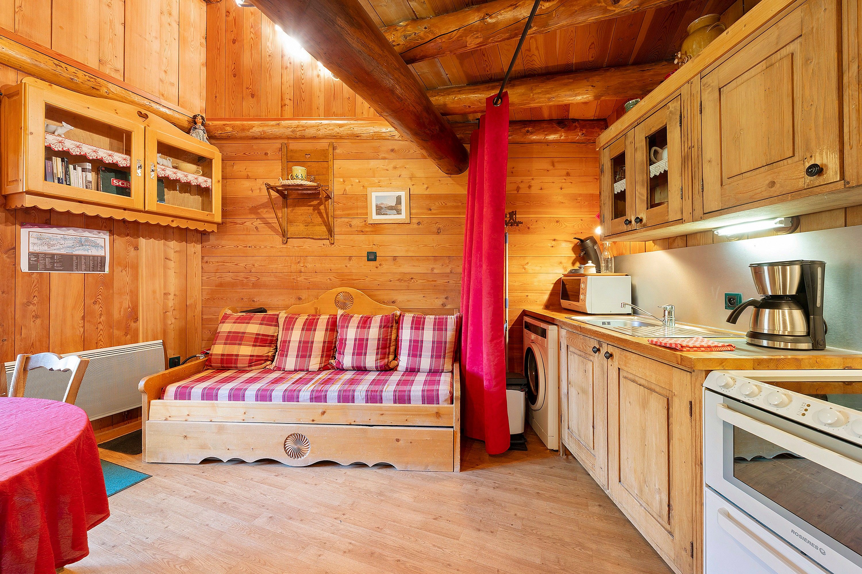 Ein gemütliches Blockhaushaus-Interieur mit einer Holzdavonia, einem Esstisch, einer Küchenzeile und einem roten Vorhang.