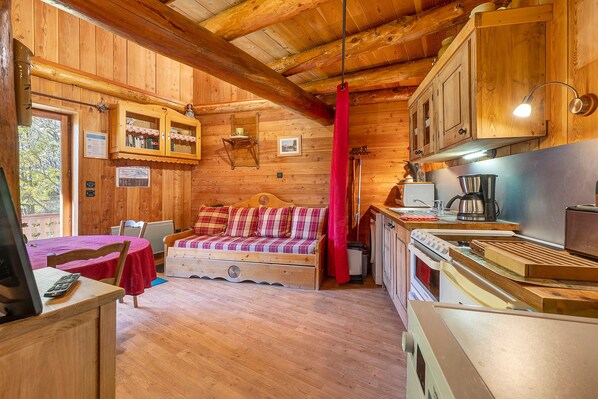 Interior acogedor de una cabaña con detalles de madera, un sofá, una mesa de comedor y una kitchenette.