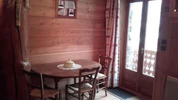 Een houten interieur met een ronde tafel, vier stoelen, een klein decoratief object op de tafel, een ingelijst beeld op de muur en een raam met gordijnen.