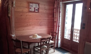 Ein Holzinnenraum mit einem runden Tisch, vier Stühlen, einem kleinen dekorativen Gegenstand auf dem Tisch, einem gerahmten Bild an der Wand und einem Fenster mit Vorhängen.