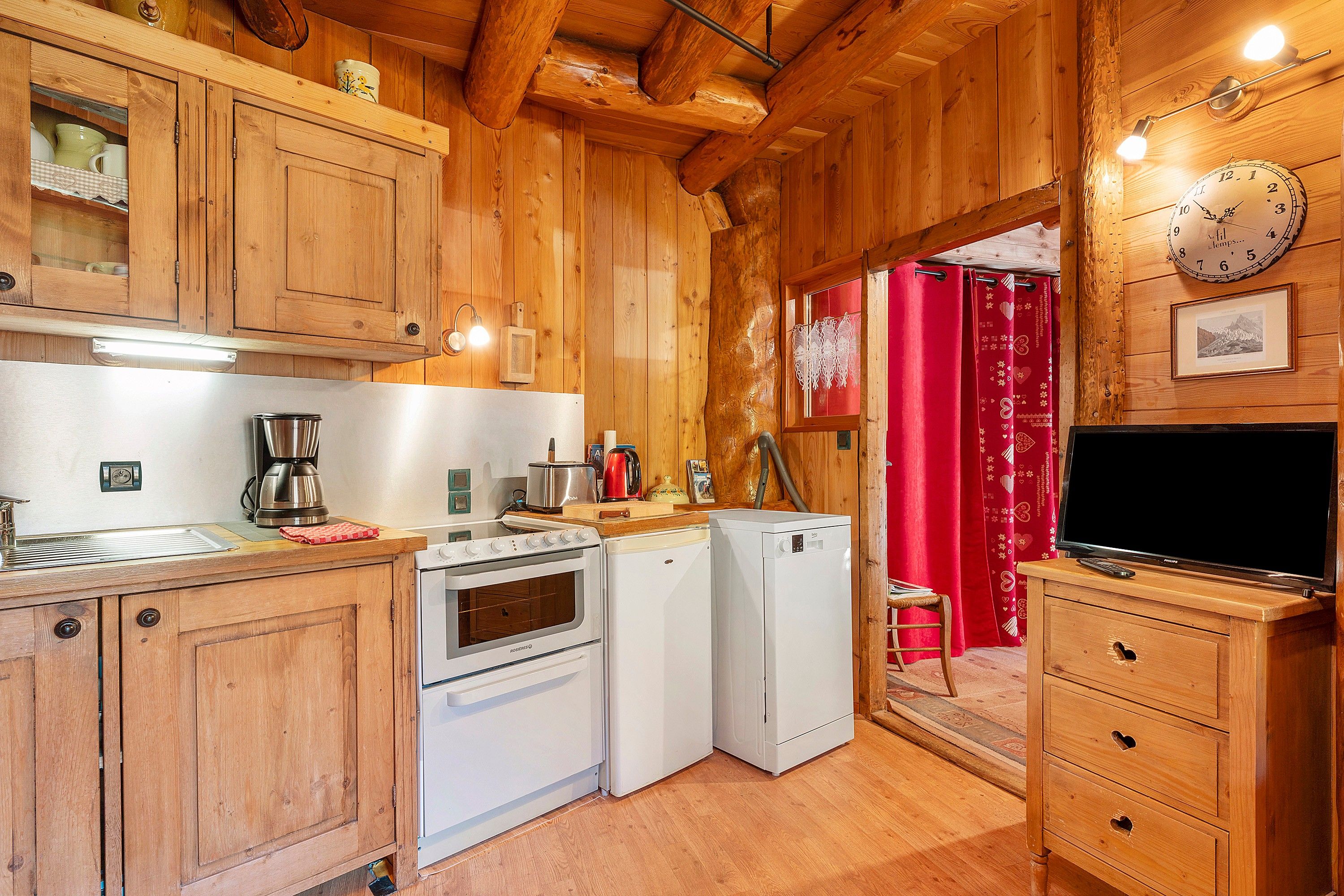 A wooden interior with a kitchen area featuring a stove, refrigerator, and coffee maker.