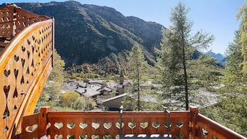 A wooden staircase with heart-shaped cutouts leading to a village with traditional buildings and a mountain backdrop.