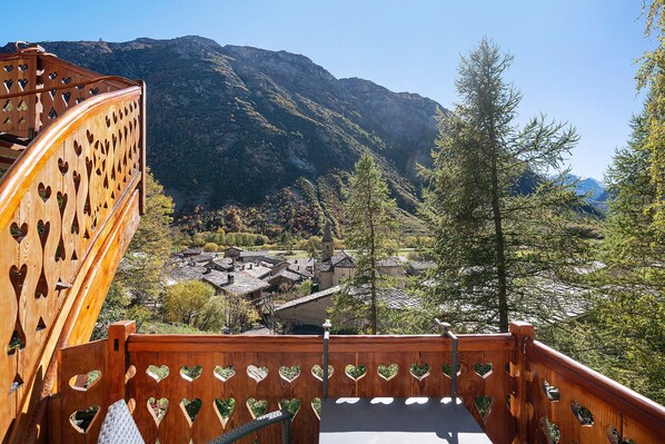 A wooden staircase with heart-shaped cutouts leading to a village with traditional buildings and a mountain backdrop.