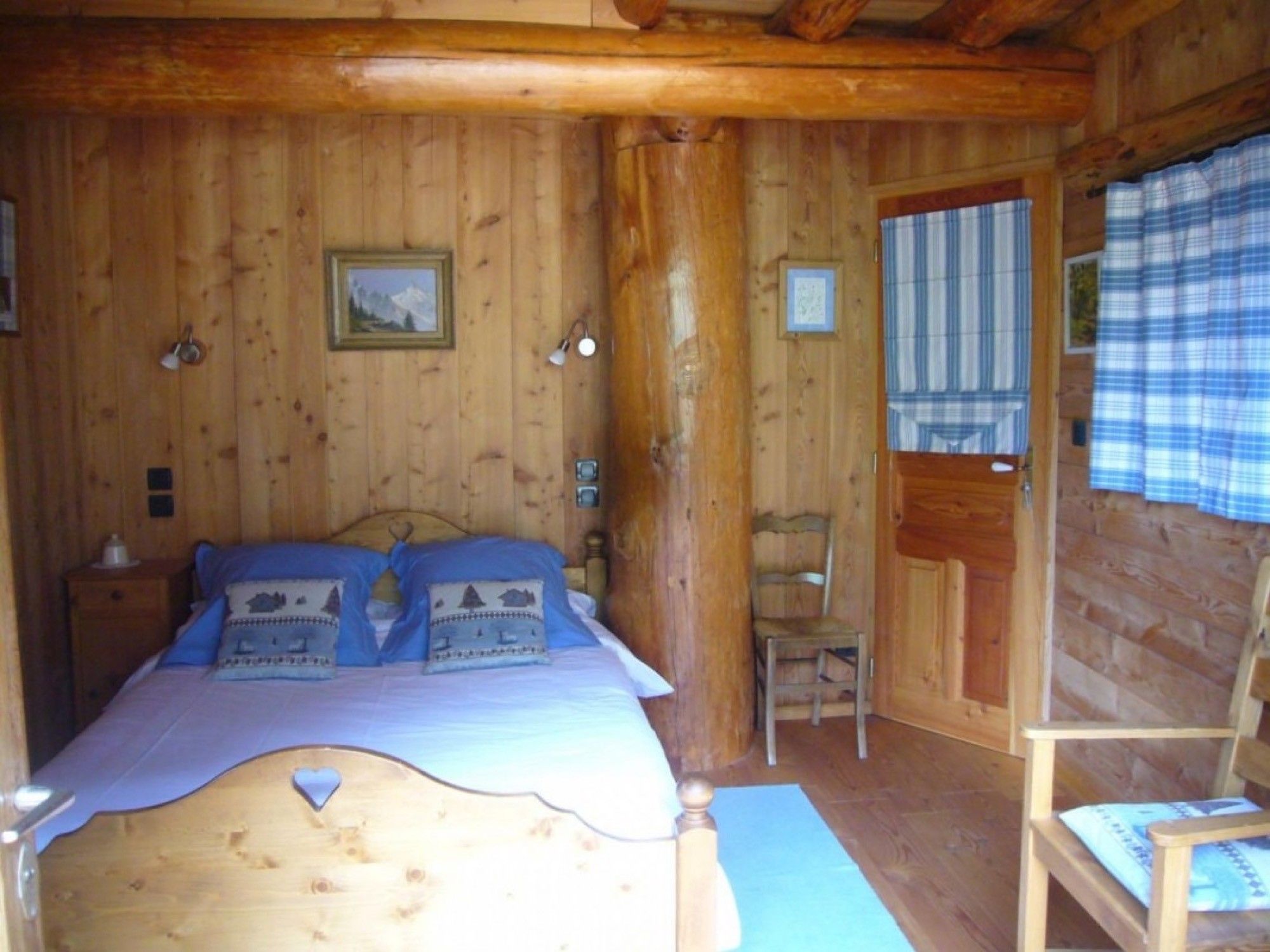 Ein Schlafzimmer einer Holzhütte mit einem Bett, einem Stuhl und einer Tür.