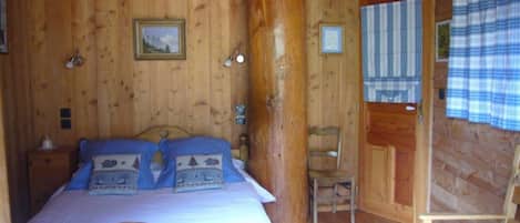 Ein Schlafzimmer einer Holzhütte mit einem Bett, einem Stuhl und einer Tür.