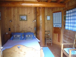 Un dormitorio de cabaña de madera con una cama, una silla y una puerta.