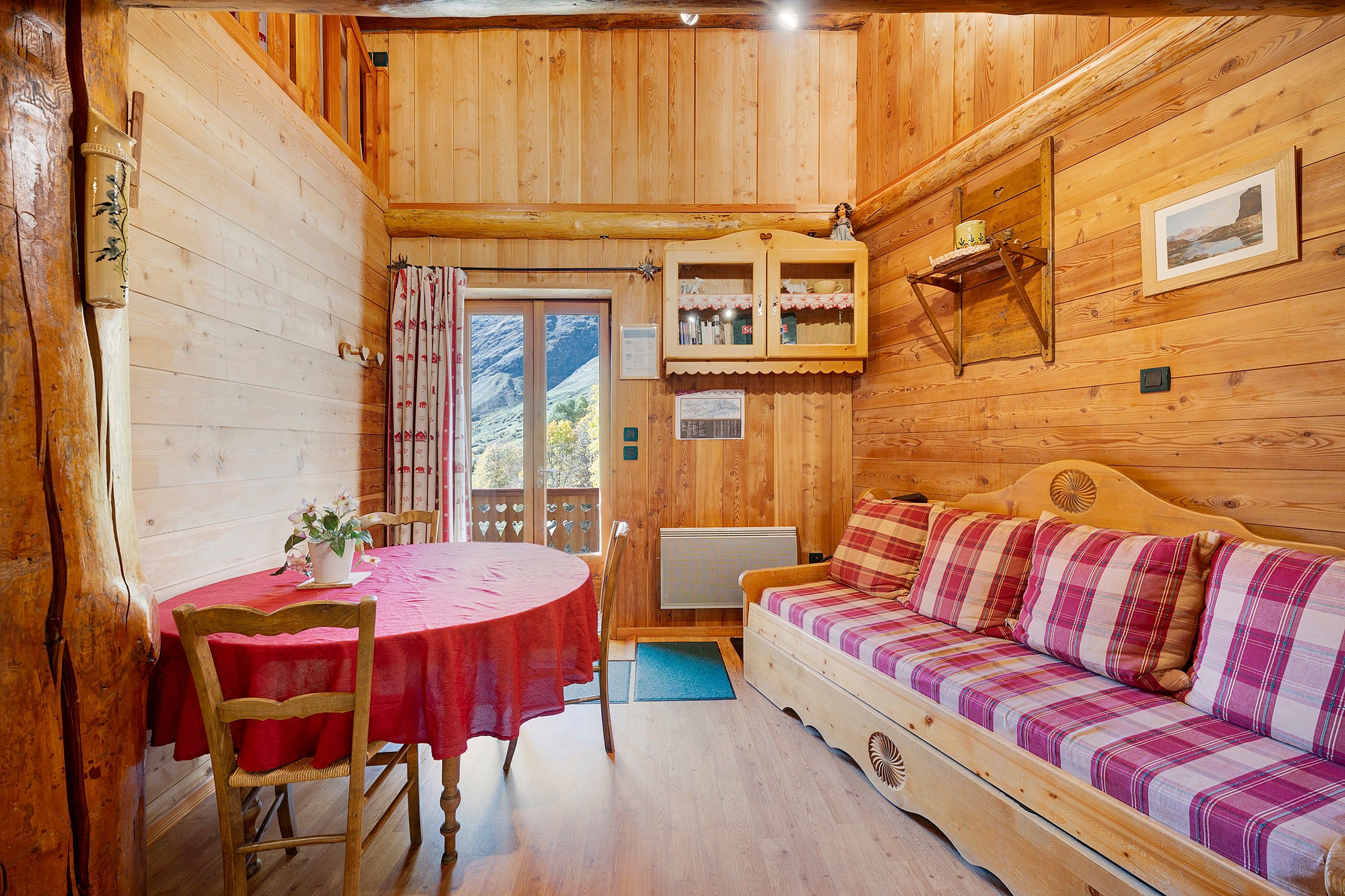 Interno di una baita in legno con un tavolo da pranzo, un divano e una finestra vista montagne.