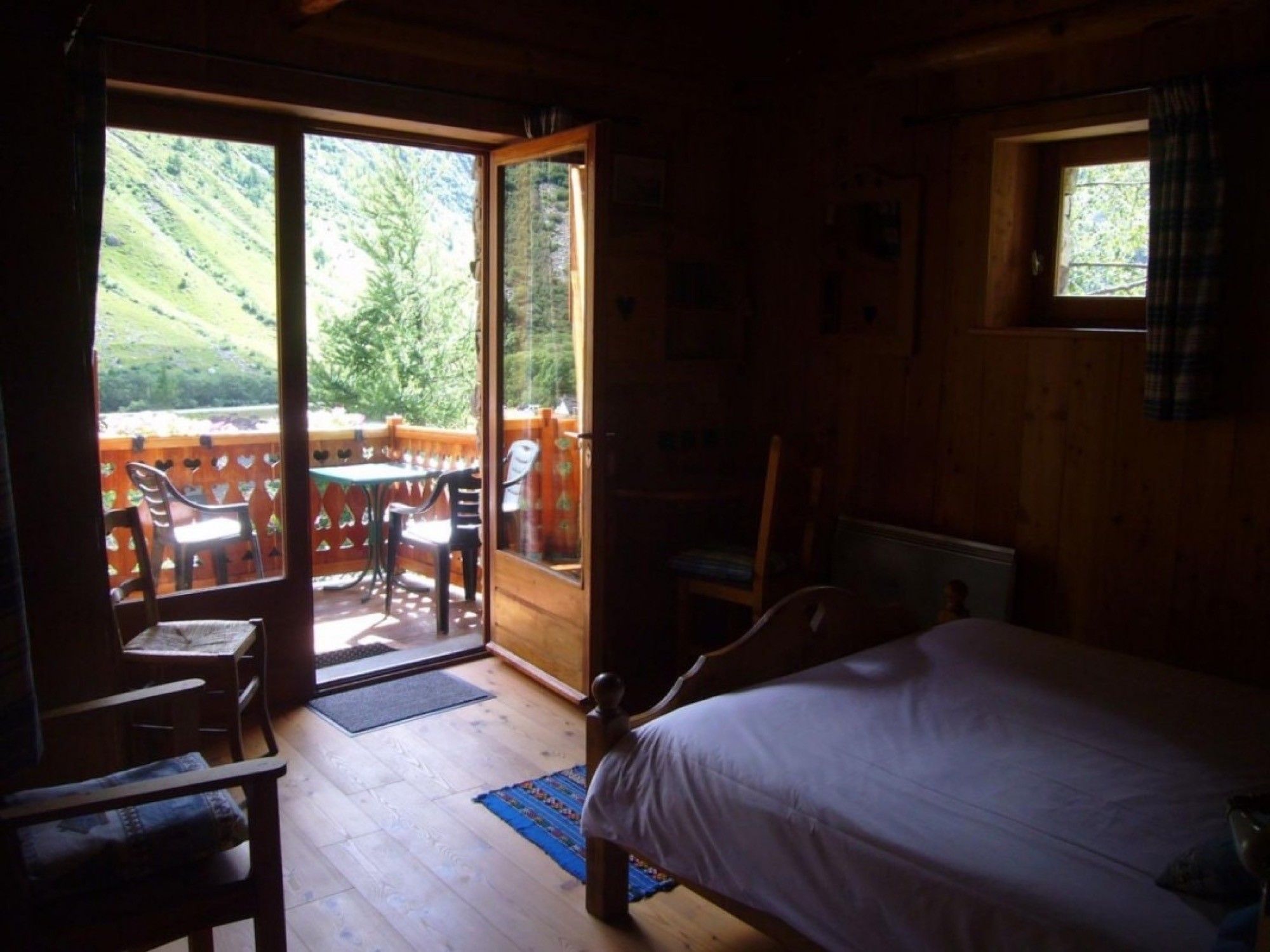 Ein Schlafzimmer mit Bett, Sessel, Tisch und Blick auf eine Terrasse mit Stühlen und Tisch.