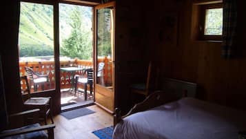 Ein Schlafzimmer mit Bett, Sessel, Tisch und Blick auf eine Terrasse mit Stühlen und Tisch.