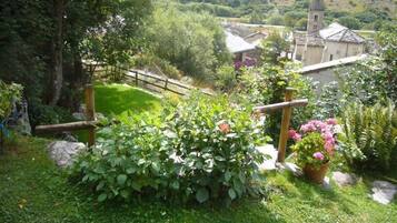 Een weelderige tuin met verschillende planten en bloemen, een houten hek en een gebouw met pannendak op de achtergrond.