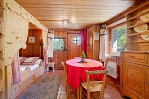 Interior acogedor de una cabaña, con paredes de madera, una mesa redonda cubierta con un mantel rojo y una cama con ropa de cama escocesa.