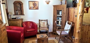 A cozy living room with a red sofa, a wooden cabinet, and a television. - Gîte Les Croës – Chalet Les Abeillos (Bonneval-sur-Arc)