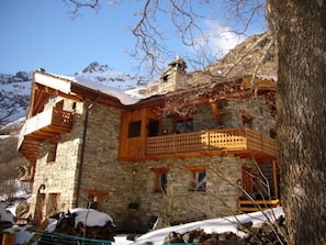 A stone building with wooden balconies and a snowy mountain backdrop. - Gîte Les Croës – Chalet Les Abeillos (Bonneval-sur-Arc)