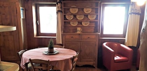 A wooden interior with a round table, chairs, a cabinet with plates, and a red armchair. - Gîte Les Croës – Chalet Les Abeillos (Bonneval-sur-Arc)