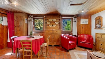 A cozy room with a wooden interior, a round table with chairs, a red sofa, and a cabinet with decorative plates.