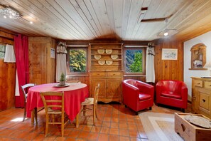 A cozy room with a wooden interior, a round table with chairs, a red sofa, and a cabinet with decorative plates.
